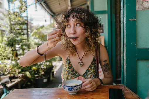 Cheerful woman who sitting in front of restaurant enjoying eating tasty Thai dessert.