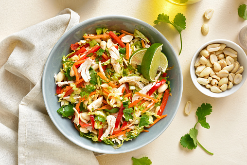 Crunchy thai style chicken salad in bowl over light stone background. Top view, flat lay