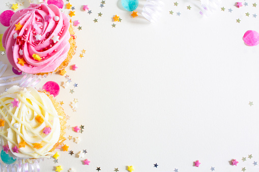 Vanilla buttercream cupcakes with pink and cream icing, sprinkles and stars on a white background.