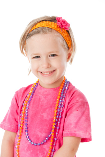 A head and shoulders image of a smiling caucasian little girl in pink wearing bright jewelry and accessories.