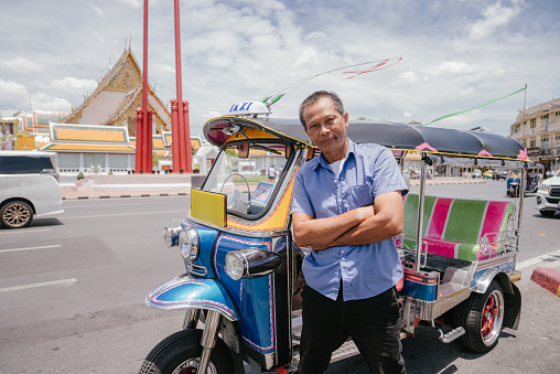 Portrait of Tuk Tuk Driver standing with his car inside the road at Bangkok old town.