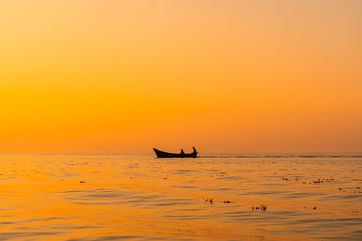 Fishing boat with a fisherman fishing in the orange sunset of Shkoder Lake in Shiroka. Albania