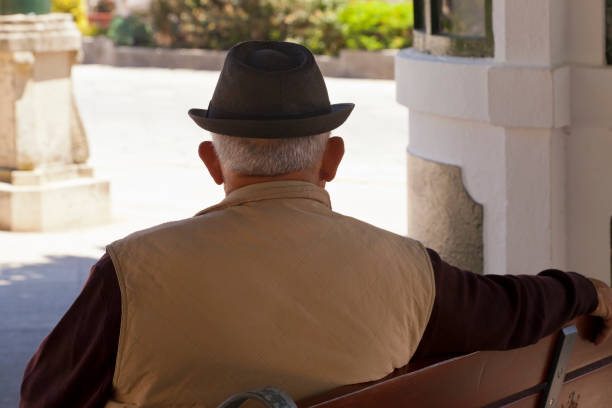Senior man wearing hat, sitting on a bench in the shadow, silhouetted. Tuy, Pontevedra province, Galicia, Spain.