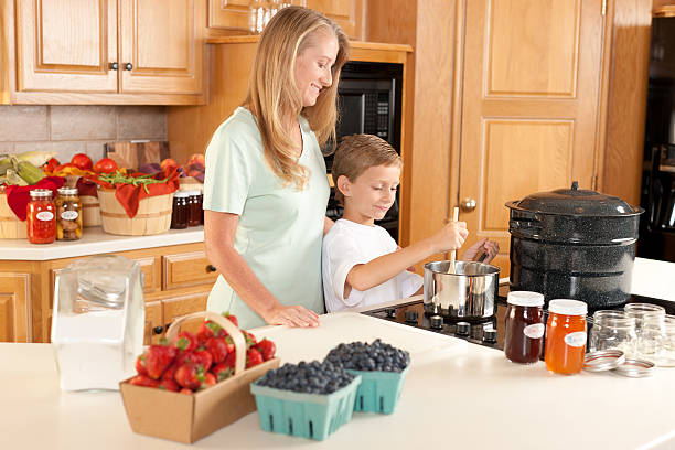 canning: mãe e filho fazendo caseiros, compotas de frutas e vegetais cultivadas no local usando - jar canning food preserves - fotografias e filmes do acervo