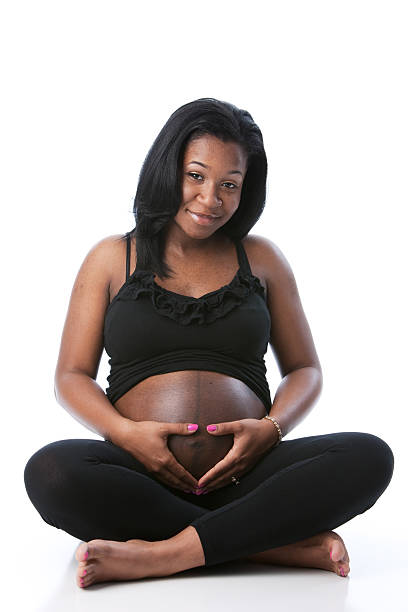 real people: black pregnant mother touching abdomen heart full length - pregnant isolated on white stockfoto's en -beelden