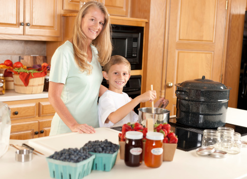 A waist up image of a caucasian mother and son canning homegrown fruits for preserves.
