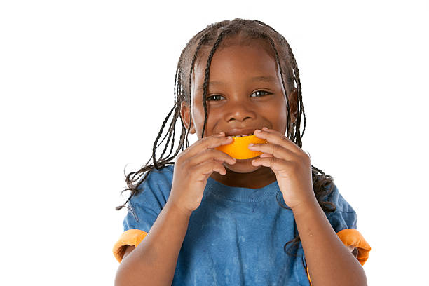 Healthy Eating: African American Little Boy Orange Mouth Fruit A head and shoulders image of an African American little boy making a happy face with an orange in his mouth for healthy eating. oranges with faces stock pictures, royalty-free photos & images