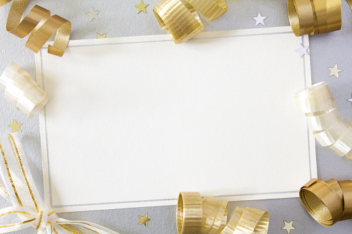 A blank card with gold and cream ribbons on a silver background, with copy space.