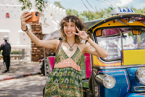 Cheerful young woman enjoying travel and selfie with smartphone near Tuk Tuk on weekend.