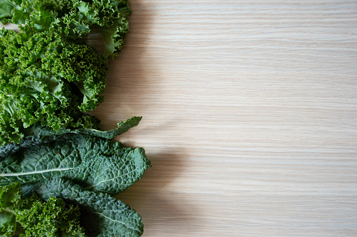 Organic curly kale leaves mix on a light wooden table, top view with space for text
