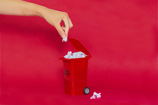 Trash can with paper inside on red background. Recycle concept.