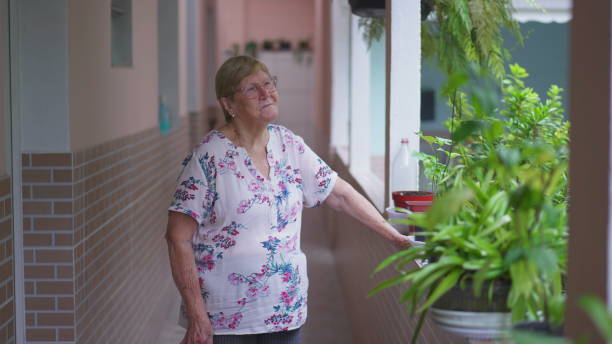 Thoughtful Elderly woman standing outside at home backyard remembering past memories. Aged 80s person in contemplation