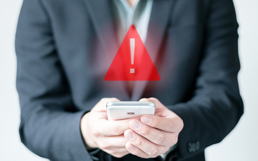 Businessman using a smartphone with a warning sign. System error hologram. Antivirus. Triangular error and caution notification. Concepts of system maintenance, privacy and data security.