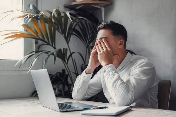 istock Stressed tired man in pain having strong terrible headache attack after computer laptop work, fatigued exhausted guy suffering from chronic migraine massaging temples to relieve head ache tension 1663929057