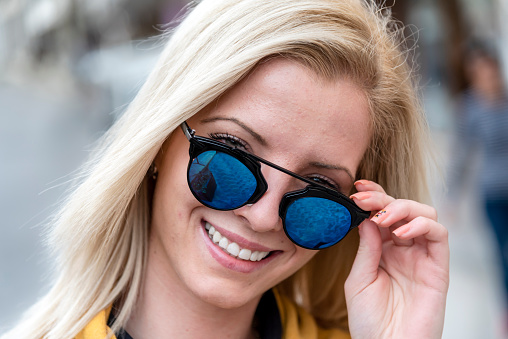Portrait of a young blond woman with sunglasses walking in the city.