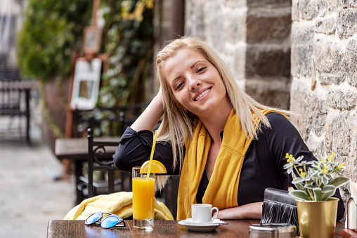 Smiling, young, blond female tourist in sidewalk cafe.