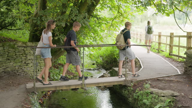 Teenagers walking over a small stream in village of Bibury
