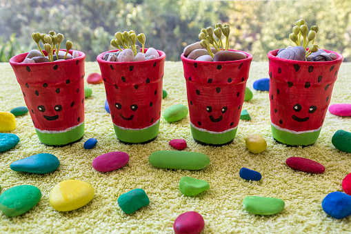 Four small watermelon painted plant pots with funny faces among colorful stones