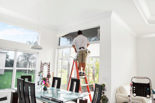 Workman on ladder agregar tinting a la parte superior de la ventana interior photo
