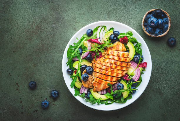 istock Delicious salad with blueberries, grilled chicken, avocado, red onion, walnuts, arugula and mixed herbs, green table background, top view 1664016577
