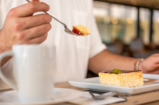 Man eating Tres Leches dessert. Close-up. Trileche. The man's face is not visible. He's wearing a white t-shirt. Trileçe is a milk dessert.