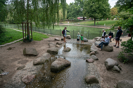 08-27-2023 Berlin Germany. View in Volkspark Friedrichshain parents and childs  and pond and small stream where kids walk barefoot in the water in summer and harden