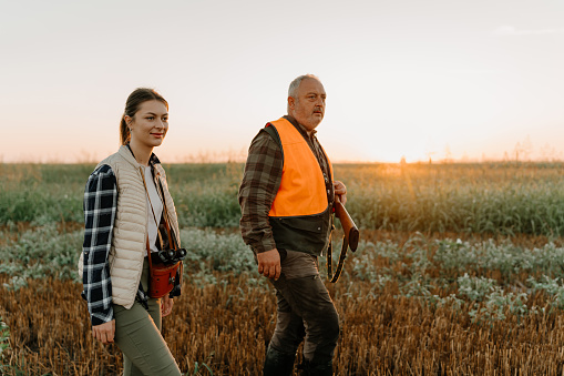 A mature Caucasian male hunter is walking with his young Caucasian daughter, while going for a morning hunt.