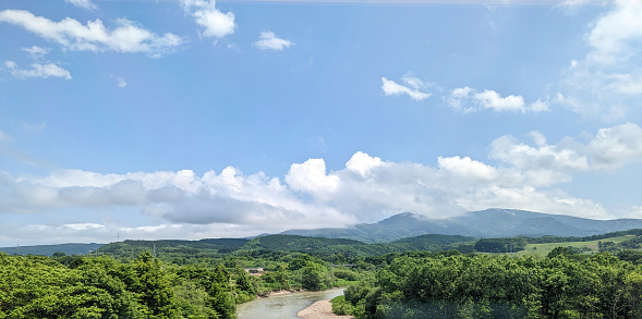 Nakanogawa with lush vegetation and mountains to the east in Kamiiso District. Spring afternoon with clouds over Oshima Subprefecture.