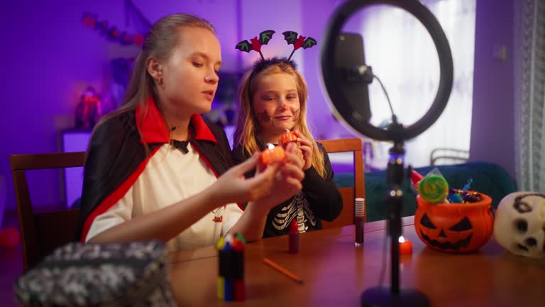 Young mother and her small daughter taking videos for social media about their Halloween decoration products at home