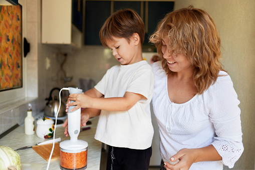 Мать учит сына готовить здоровую пищу на кухне. Ребенок учится готовить.