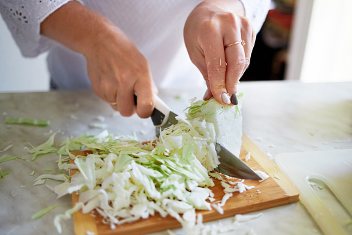 Женские руки нарезают капусту. Приготовление здоровой пищи дома.