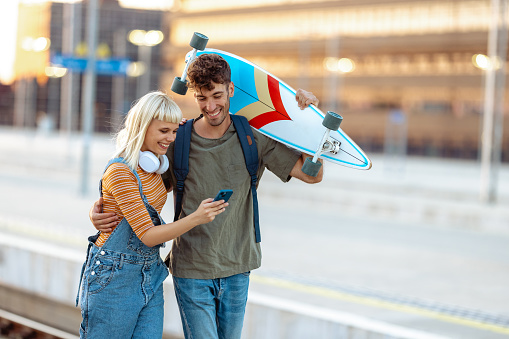 Young woman and man using smart phone in the city and cheerfully walking on a railroad station