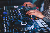 View of Dj mixer and vinyl plate with headphones on a table with DJ playing and mixes the track in the background, during night techno party in nightclub