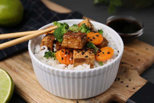 bol de riz avec tofu frit, brocoli et carottes sur planche de bois, gros plan - tofu chinese cuisine vegetarian food broccoli photos et images de collection