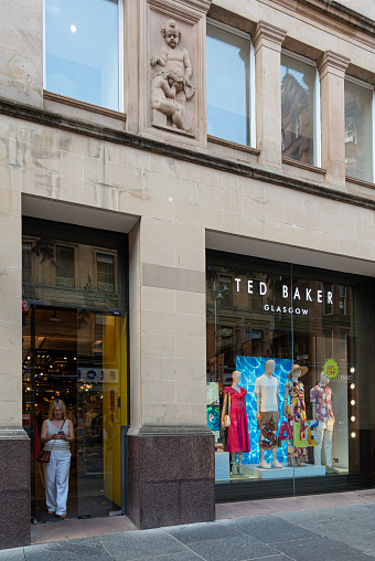 Glasgow, Scotland, UK - 16th June 2023: Woman looking at her phone while leaving the Ted Baker clothing shop in Buchanan Street, Glasgow. Ted Baker is a UK company headquartered in London and is part of the US-based Authentic Brands Group LLC