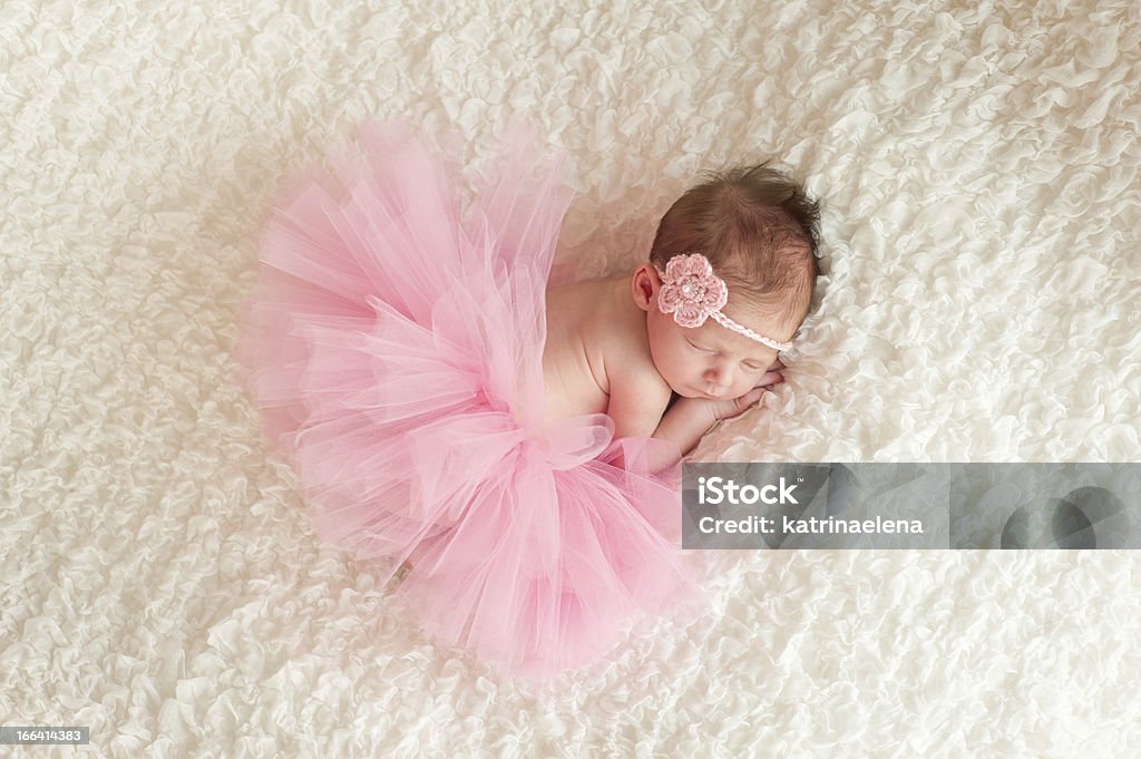 Newborn Baby Girl Wearing a Pink Tutu An overhead view of a sleeping newborn baby girl wearing a pink crocheted headband and tutu. She is sleeping on white billowy fabric. 0-11 Months Stock Photo