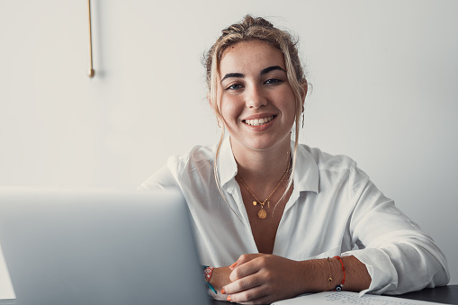 Good-looking millennial office employee student sitting at desk in front of laptop smiling looking at camera. Successful worker, career advance and opportunity, owner of prosperous business concept