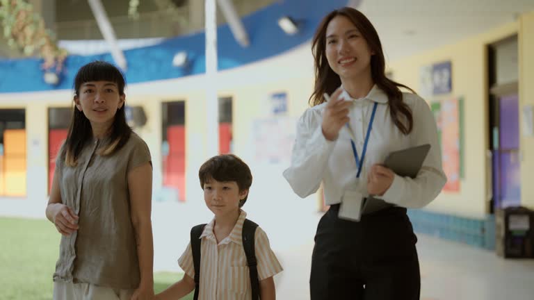 Asian parents and cute son explore new school with teacher at popular summer school opening event.