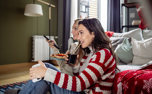 Two young woman watching TV at home. They are eating pizza and relaxing.