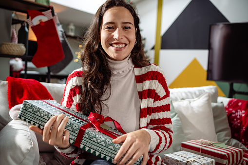 Young woman at home, holding Christmas present, looking at camera and smiling