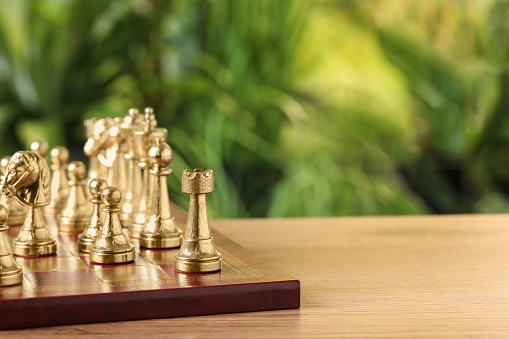 Chess board with golden pieces on wooden table against blurred background, space for text