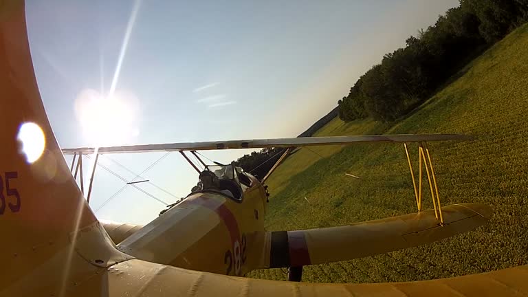 Yellow Biplane Flying Low over Farmland and a House