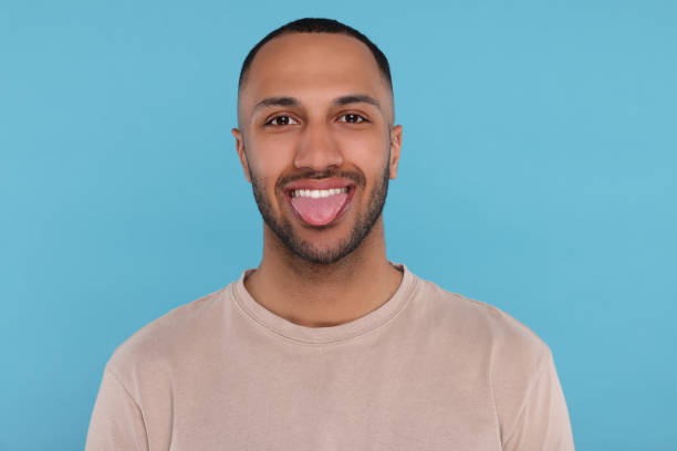 istock Happy young man showing his tongue on light blue background 1664207577