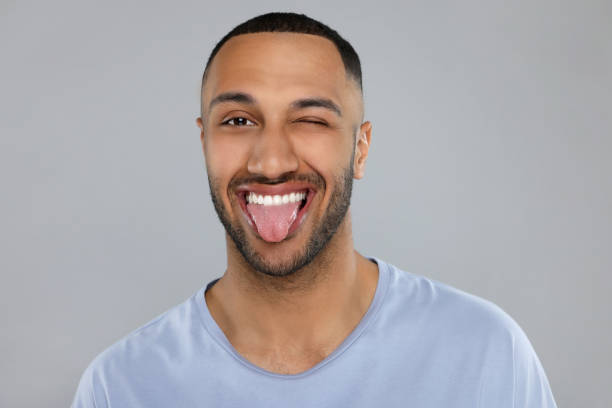 istock Happy young man showing his tongue on light grey background 1664207969