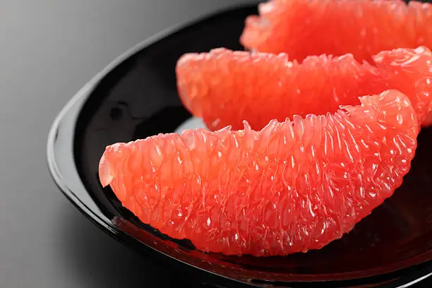 Three slices of fresh grapefruit on a black plate. Black background. Close-up.