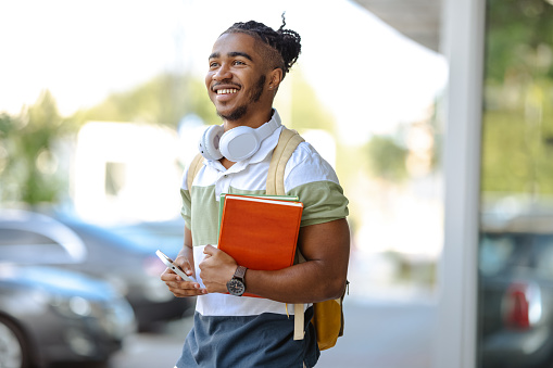 Smiling male student holding books and backpack