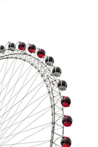 A photo of from antalya, Turkey. a Ferris wheel with red and white passenger cars. The Ferris wheel is made of steel and has a white frame. The passenger cars are red and white and are attached to the frame with cables. The background is white and the image is taken from a low angle, looking up at the Ferris wheel. The image is cropped so that only part of the Ferris wheel is visible.