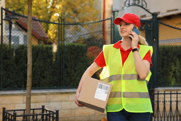 istock Courier in uniform with parcel talking on smartphone near private house outdoors, space for text 1664294242