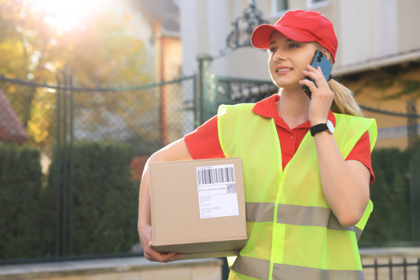 istock Courier in uniform with parcel talking on smartphone near private house outdoors, space for text 1664295261