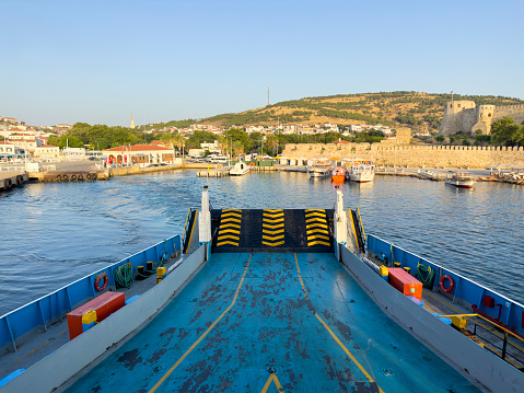 Sunny summer morning, the empty car ferry leaves the port of Bozcaada. Bozcaada castle and town view in the background. No people. A Turkish island in the North Aegean Sea